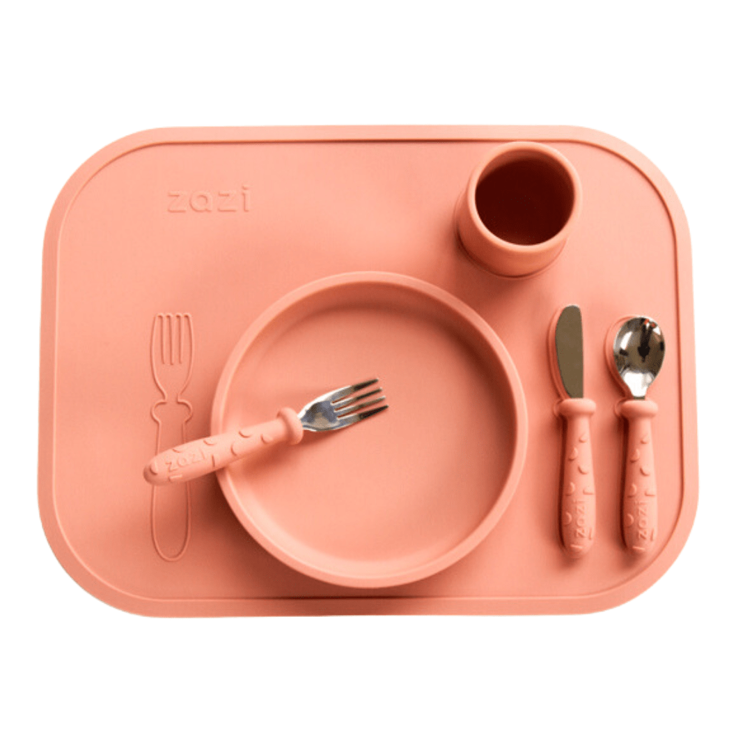 The Zazi Clever Mat dinner set for children comes in pink and includes a plate, cup, fork, knife, and spoon. All items are made from food-grade silicone and designed to be arranged on the matching Clever Mat with suction technology.