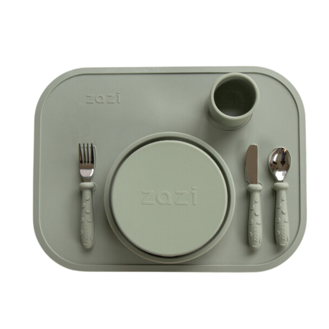 The Zazi Clever Mat gray silicone baby dining set includes a mat, fork, spoon, plate, bowl, and cup. All pieces are crafted from food-grade silicone and labeled "Zazi," ensuring easy cleaning and secure placement with innovative suction technology.