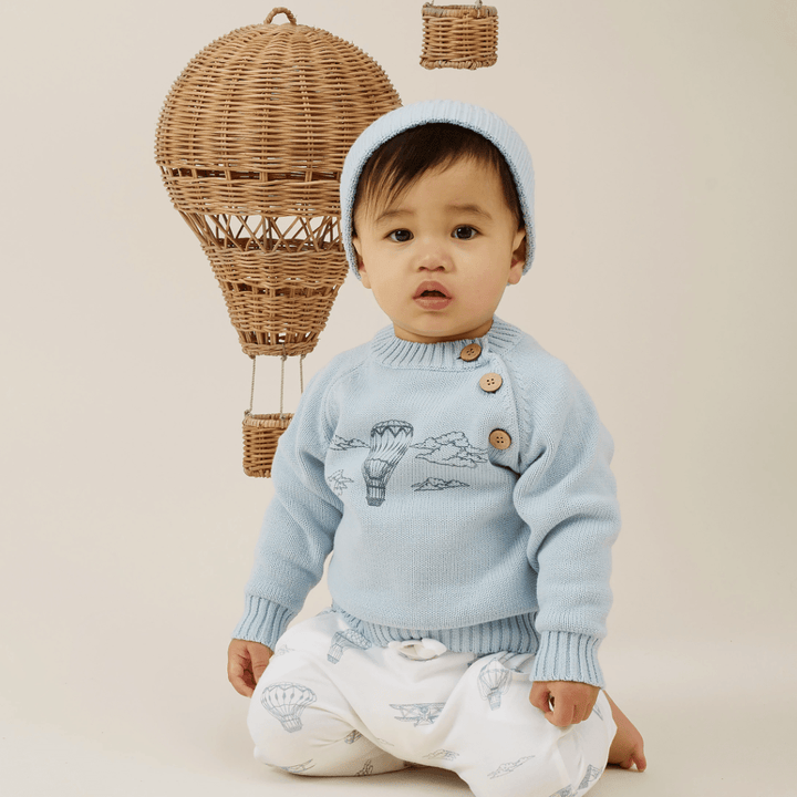 A toddler in Aster & Oak organic harem pants sits against a backdrop of woven wicker hot air balloons.