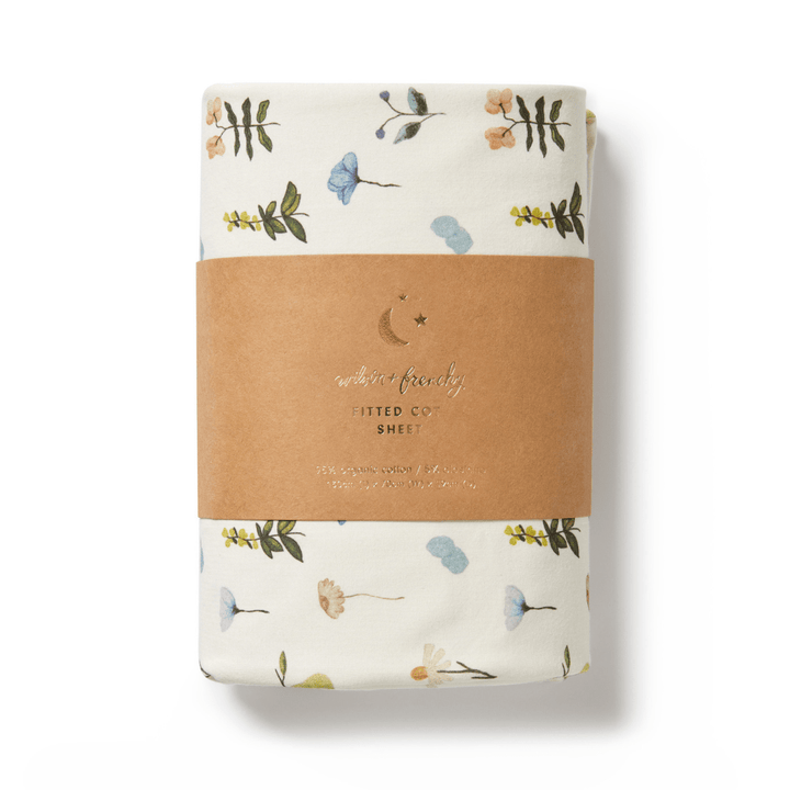 A folded fitted cot sheet made from organic cotton with tribal patterns, wrapped in a brown paper label that reads "Wilson & Frenchy Organic Cotton Cot Sheet - LUCKY LAST - TRIBAL WOODS ONLY"—a perfect GOTS-certified baby shower gift.