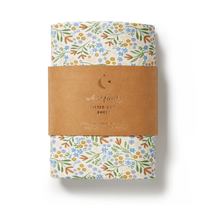 A rolled-up Wilson & Frenchy Organic Cotton Cot Sheet in the exclusive Tribal Woods pattern, wrapped in a brown paper band labeled "Fitted Cot Sheet," featuring white, blue, and green colors. This GOTS-certified cot sheet makes a perfect baby shower gift.