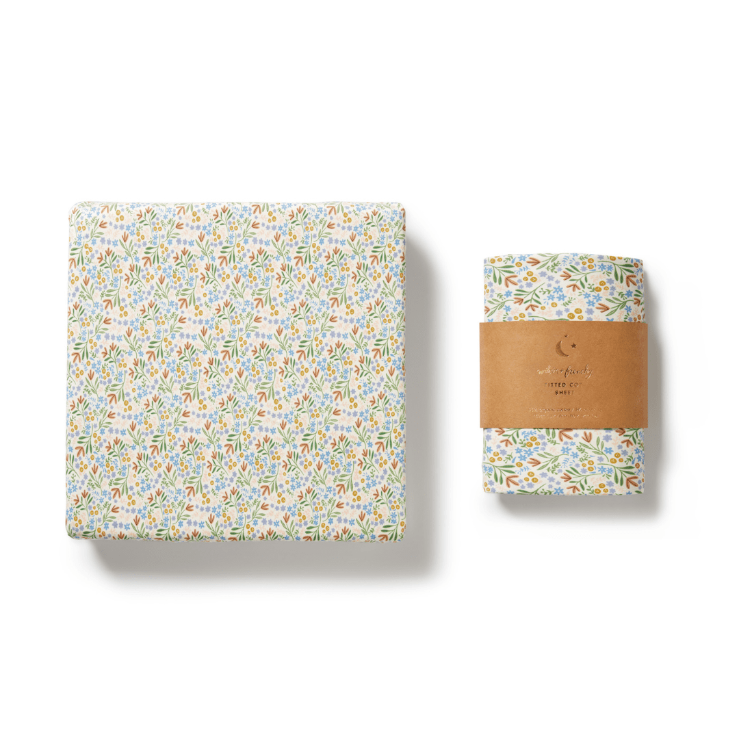 Wilson & Frenchy gift box in a tribal woods pattern next to a matching Wilson & Frenchy Organic Cotton Cot Sheet wrapped with a brown paper band, perfect for a baby shower gift. The cot sheet is GOTS-certified and isolated on a white background.