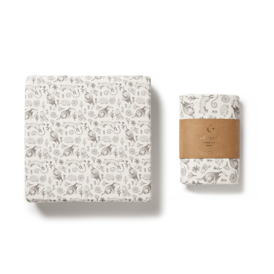 A Wilson & Frenchy Organic Cotton Cot Sheet - LUCKY LAST - TRIBAL WOODS ONLY, wrapped in a brown paper band alongside a patterned square box, both showcasing delightful nature-themed designs with animals and plants—a perfect baby shower gift.