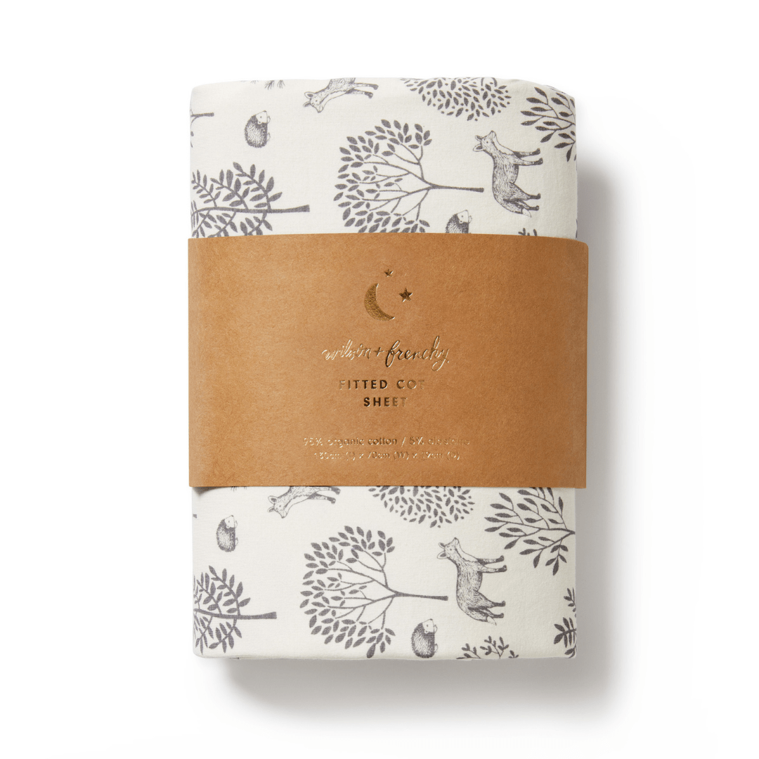 A packaged Wilson & Frenchy Organic Cotton Cot Sheet - LUCKY LAST - TRIBAL WOODS ONLY with nature-themed illustrations, including trees and animals, wrapped with a brown paper band labeled "Fitted Cot Sheet" – an ideal baby shower gift.