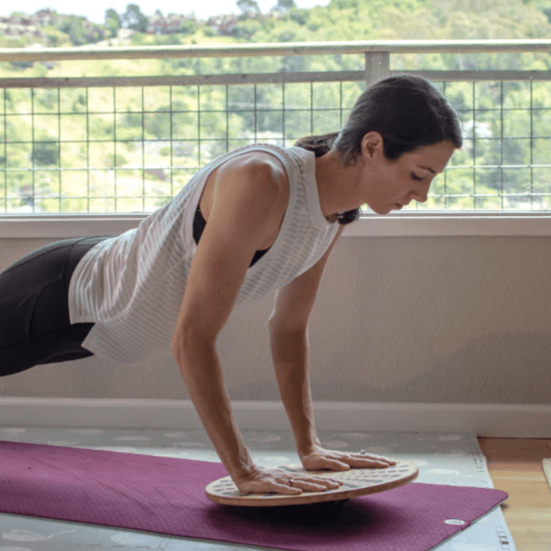 An eco-friendly woman doing a plank on a Kinderfeets Bamboo Balance Disk yoga mat.