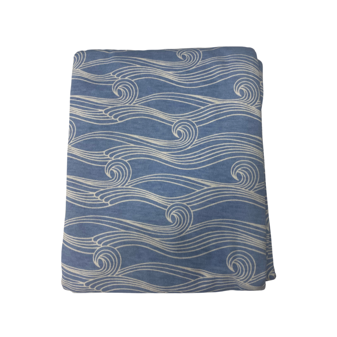 The Woolbabe Merino & Organic Cotton Swaddle Blanket by Woolbabe features folded blue fabric crafted from soft organic cotton, accented with a delicate white wave pattern design.