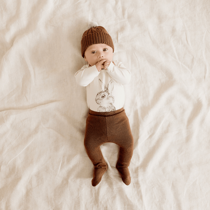 Baby-Lying-Down-Wearing-Wilson-and-Frenchy-Knitted-Leggings-with-Feet-Dijon-with-Bunny-Onesie-Naked-Baby-Eco-Boutique