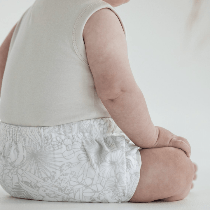 A baby wearing a sleeveless onesie and Aster & Oak Organic Animal Bloomers - LUCKY LASTS - 3-6 MONTHS & 6-12 MONTHS ONLY is sitting on the floor.