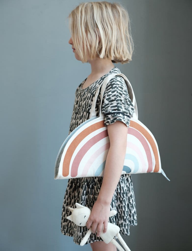 A little girl in a white dress holding a Fabelab Organic Cotton Play Purse made of organic cotton.